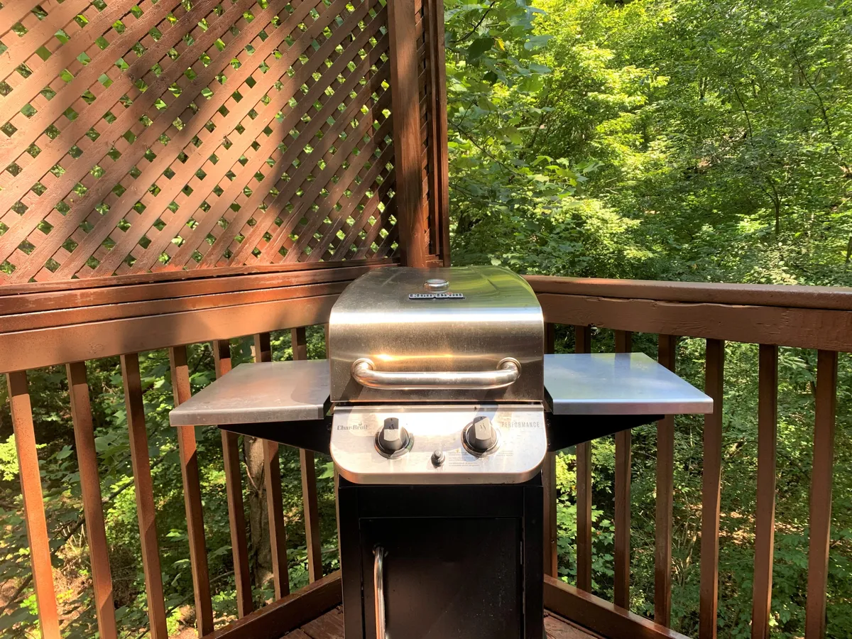 An inviting outdoor area featuring a gas BBQ grill positioned by a wooden railing and latticework. The setting is ideal for outdoor cooking and casual gatherings, with the grill ready for use and ample space for socializing amidst lush greenery.