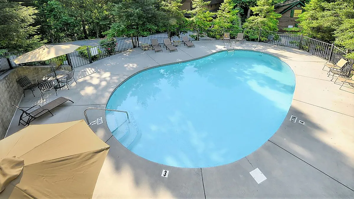 A sparkling shared outdoor pool area, complete with lounge chairs, umbrellas, and landscaped greenery. Guests are shown sunbathing and socializing, evoking a vibrant, communal summer experience.