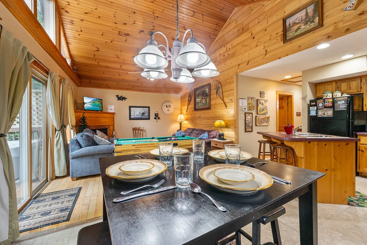 A welcoming cabin interior with a dining table set for a meal, a pool table, and a comfortable sofa area. The space exudes a relaxed, sociable atmosphere perfect for unwinding after a day outdoors. The arrangement of furniture highlights opportunities for group gatherings and leisure.