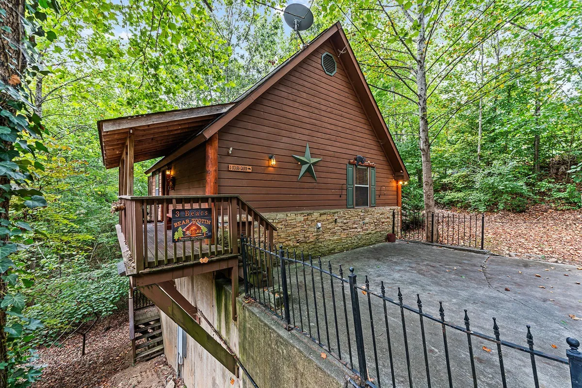 A charming, rustic wooden cabin exterior with a welcoming front porch adorned with a decorative star. The setting is tranquil, surrounded by natural greenery, hinting at a peaceful getaway close to family attractions. The porch invites outdoor relaxation and sets the stage for family gatherings and nature exploration.