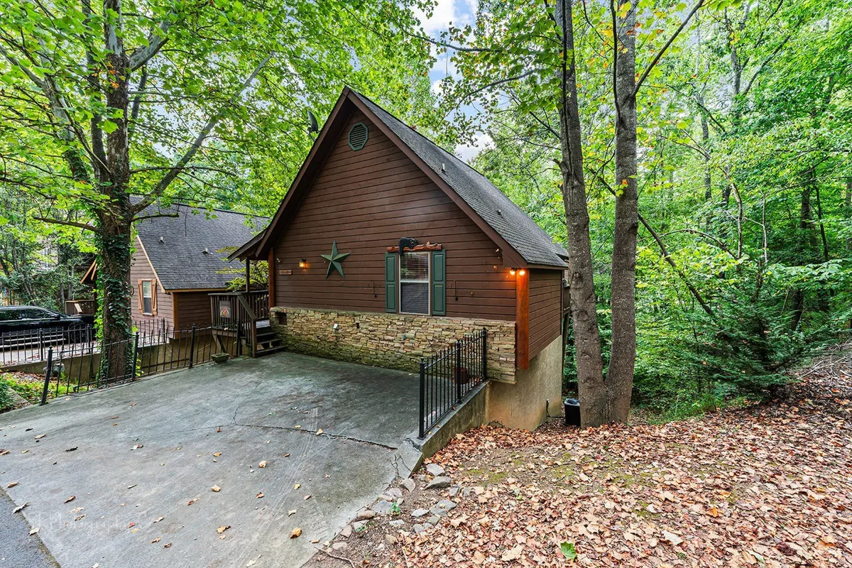 A welcoming exterior shot of a wooden cabin with a stone foundation, nestled in lush green foliage and adorned with a decorative star. The yard and surrounding nature create an inviting, peaceful atmosphere ideal for outdoor relaxation or quiet moments together.
