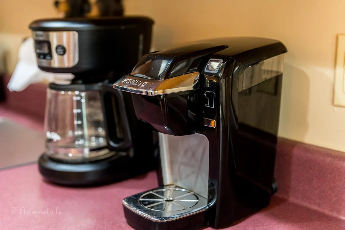 A close-up view of coffee makers, including a Keurig and a traditional coffee pot, set in a bright kitchen corner. The scene is filled with the warmth of morning rituals, inviting guests to picture themselves brewing coffee and enjoying the aroma at the start of the day.