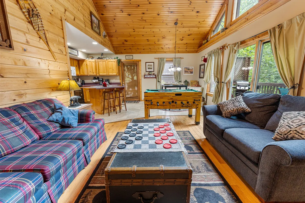 This image showcases a plaid couch and coffee table set with a checkers game, a foosball table, and large windows that fill the room with natural light. The space feels lively and inviting, capturing a playful atmosphere ideal for group gatherings and family fun.
